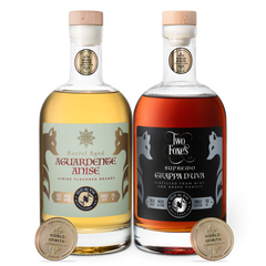 Two bottles of aged aguardente anise and grappa d'uva with labels and San Francisco World Spirits Competition gold medals on a white background