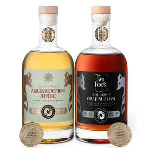 Two bottles of aged aguardente anise and grappa d'uva with labels and San Francisco World Spirits Competition gold medals on a white background