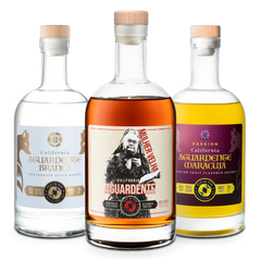 Three different style bottles of SLO de Vie aguardente on a white background